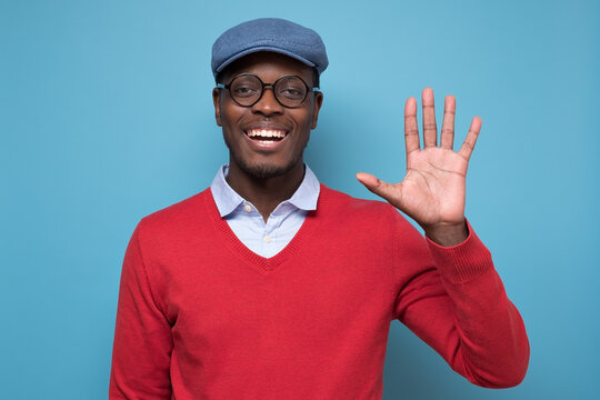 African young man with blue hat saying hello, waving a hand