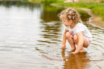 Little cute girl hsitting in the water in the river at summer. copy space
