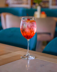 A glass with the red citrus cocktail. Alcohol summer beverage in a wine glass. Refreshing drink with ice.
