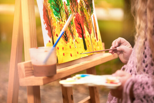 little girl artist paints a picture on an easel in autumn in the park