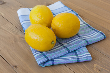 Three yellow lemons on a light checkered napkin. Three lemons on a wooden background.