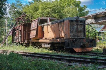 Fototapeta na wymiar Old diesel locomotive with broken wooden cargo wagon on railway