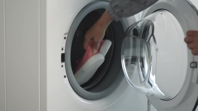 Close up of woman taking shoes from washing machine and putting them in dryer