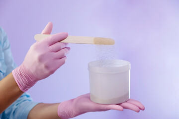 Hands of a specialist of a beauty salon pouring powder into plastic pot with a putty knife