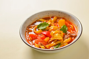 Bowl of minestrone pasta soup, served in a white bowl over bright pastel yellow background. Copy space design banner.