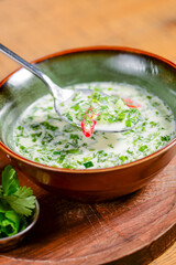 Popular spring and summer cold soup okroshka. Okroshka in a bowl, lemon and herbs on rustic wooden table.