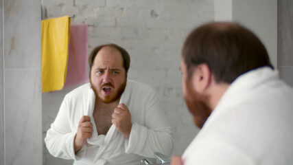 Funny overweight man in bathrobe looking in bathroom mirror and dancing - obrazy, fototapety, plakaty