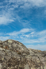 Small white seagull flying in clouds of blue sky shot from a texture rocks of island on Ladoga lake in Karelia