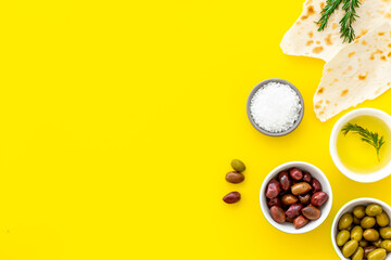 Top view of olives, olive oil, bread on yellow table top view copy space
