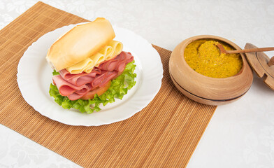 Mortadella and lettuce sandwich, on a white plate and a bamboo mat and pepper sauce and mustard on a table with white towel, selective focus.