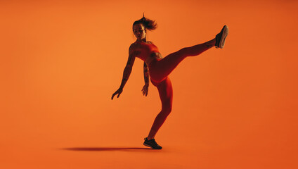 Fit woman doing leg stretches on orange background