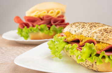 Mortadella, lettuce and cheese sandwiches and pepper and mustard sauce on white plates on a table with beige patterned tablecloth, Selective focus.