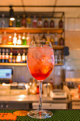 A glass with the red citrus cocktail. Alcohol summer beverage in a wine glass. Refreshing drink with ice.