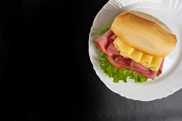 Mortadella sandwich, lettuce and cheese on a white plate on a table with black tablecloth, Top view.
