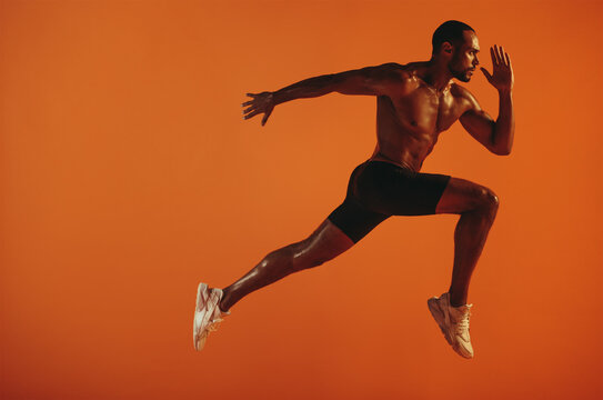 Muscular athlete running on orange background