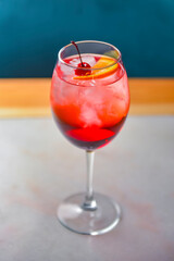 A glass with the red citrus cocktail. Alcohol summer beverage in a wine glass. Refreshing drink with ice.