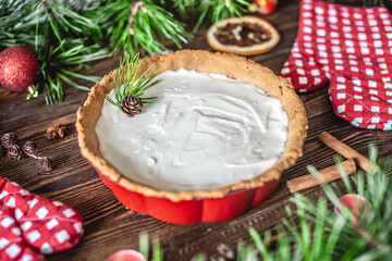 Homemade tart with white cream on wooden table decorated with pine branches. Table decoration for...