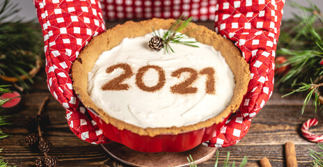 Homemade tart with the number 2021. Wooden table decorated with pine branches and red decor for Christmas and new year