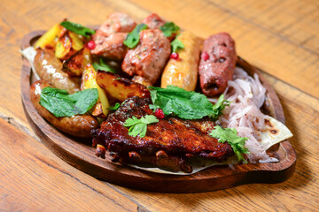 Georgian dinner. Meat, sausages and baked potatoes with fresh greenery served on a wooden board.