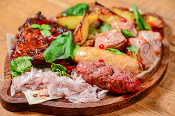 Georgian dinner. Meat, sausages and baked potatoes with fresh greenery served on a wooden board.