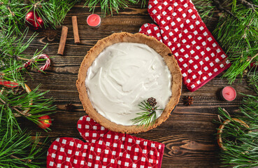 Homemade tart with white cream on wooden table decorated with pine branches. Table decoration for Christmas and new year