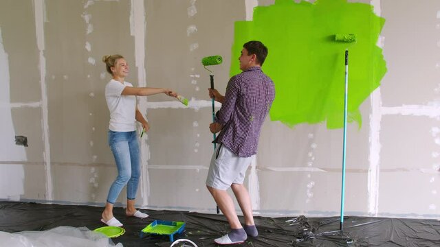 A young family dances to music during the renovation. Man and woman dancing with brushes and rollers