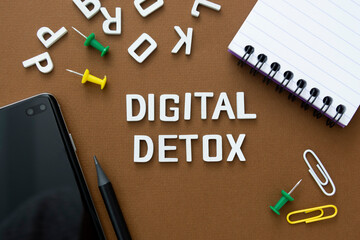 Digital detox word with smart phone, note book, office suplies over brown background.