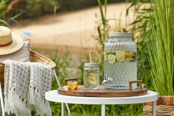 Stylish composition of outdoor garden on the lake with design rattan armchair, coffee table, plaid, pillows, drinks and elegant accessories. Summer chillout mood.