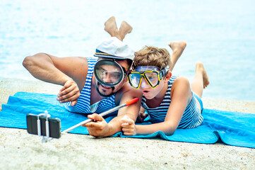 Dad and son fool around and take pictures of selfies in diving masks on the seashore. A man and a boy are having fun leisure time together. Summer travel. Summertime at the sea. Sports and recreation