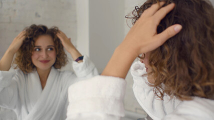 Woman touching hair and smiling looking in mirror in bathroom