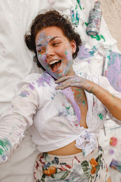 Woman with paint brush soiled in colors having fun after painting wall and home repair, lie on the flour