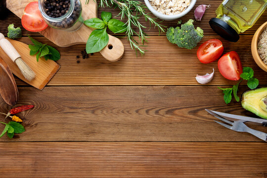Food frame, cooking mockup. Tomatoes, herbs, oil, cutting board, broccoli, pepper, kitchen utensils. Wooden background, copy space.
