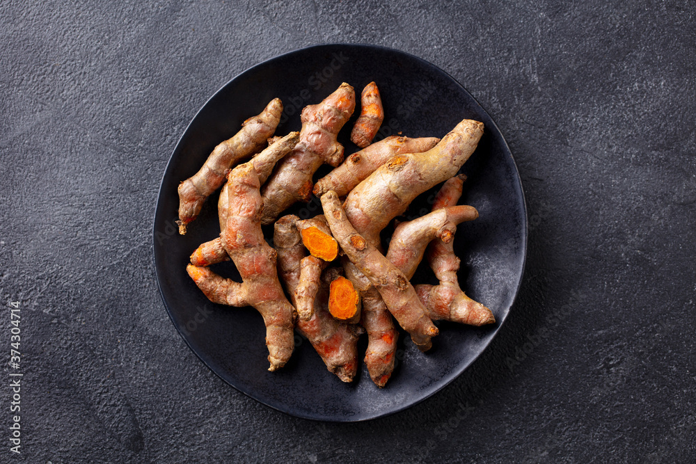 Wall mural Fresh turmeric, curcumin, tumeric roots on a black plate. Superfood product. Dark background. Close up. Top view.