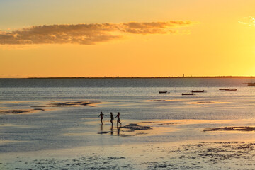 Three childrens are playing in the sea at low tide on a background of amber sunset