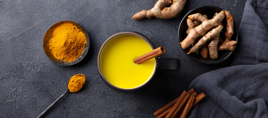 Turmeric drink, latte, tea, milk with cinnamon in a mug with fresh and powder turmeric. Dark background. Top view.