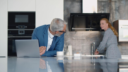 Senior businessman working on laptop and having coffee for breakfast in kitchen