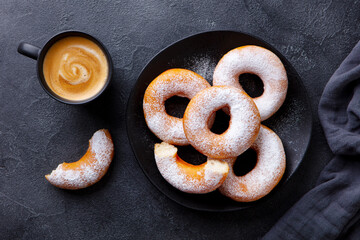 Donuts with sugar powder on black plate with cup of coffee espresso. Dark background. Top view.