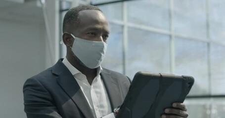 Businessman wearing face mask and working on digital tablet in office lobby - Powered by Adobe