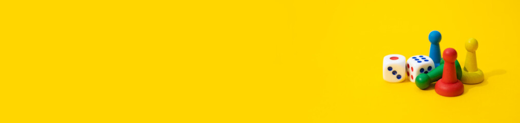 Colorful game chips and two dice are laid out on a yellow background: entertainment, games at home for the whole family, the concept of Board games. Board game. Table games, banner, space for text