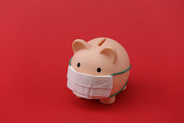 Piggy bank with medical mask on red background. Economic disease. Financial crisis. Covid-19 pandemic