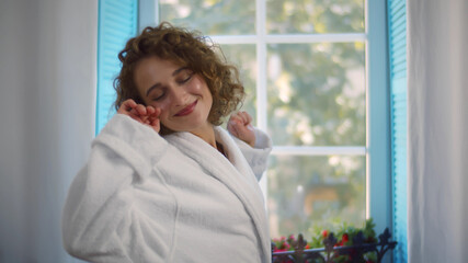 Happy woman in bathrobe stretching at window in morning