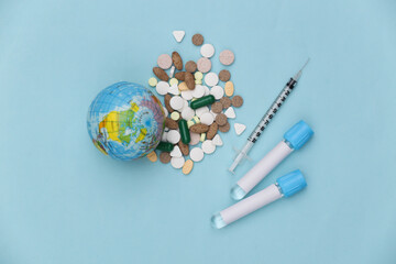 Pills with Medical test tubes, globe, syringe on blue background. Treatment. Covid-19 pandemic. Top view