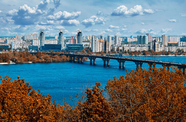Fototapeta premium City skyscrapers on the river bank. The bridge over the big river. Tall buildings. A working day in the city. Green summer trees.