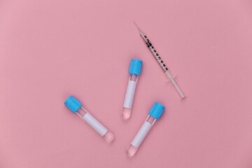 Medical test tubes with syringe on pink pastel background. Top view