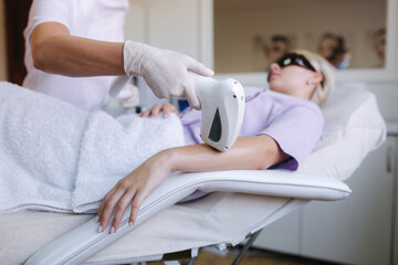 Beautician doing epilation on beautiful woman's hand in medical center. Female receiving laser light hair removal treatment for hairless smooth skin at cosmetology salon. Close up
