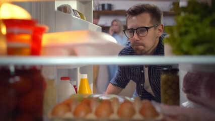 Young handsome man opening fridge and looking at container with food.