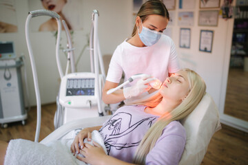 Beautiful female patient is getting a face skin treatment while lying at medical clinic