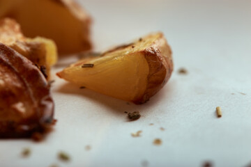 Some delicious baked potatoes slices with seasoning on white paper cutting board and wooden table background from side close up
