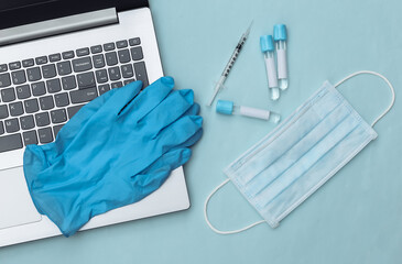 Medical test tubes, face mask, gloves with syringe and laptop on blue background. Top view