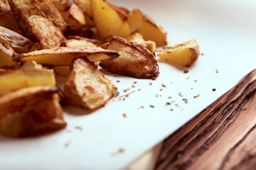 Delicious baked potatoes slices with seasoning on white paper cutting board and wooden table from side close up